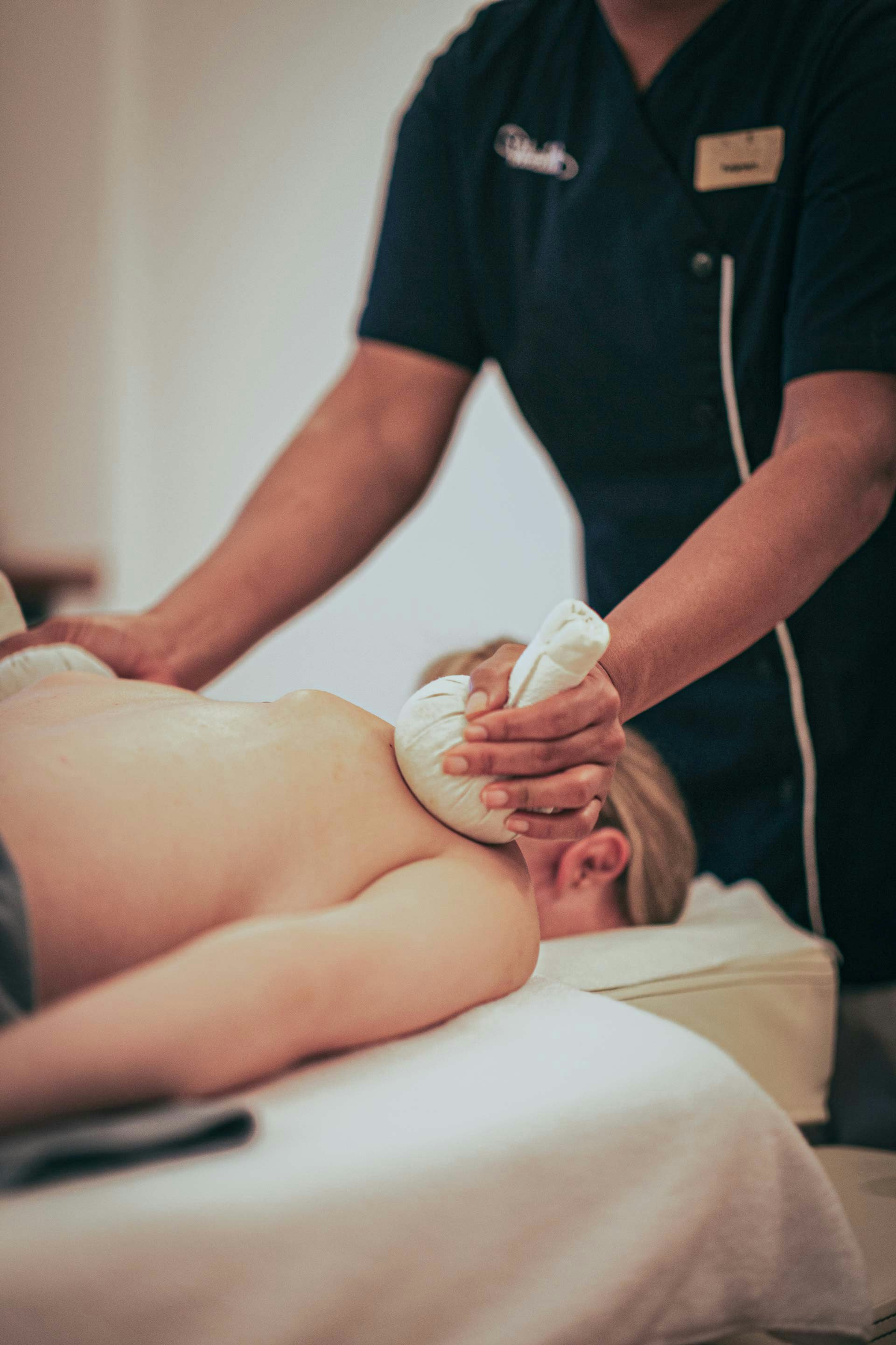 Eine Frau liegt auf dem Bauch auf einer Massageliege und wird mit Kräuterstempeln massiert
