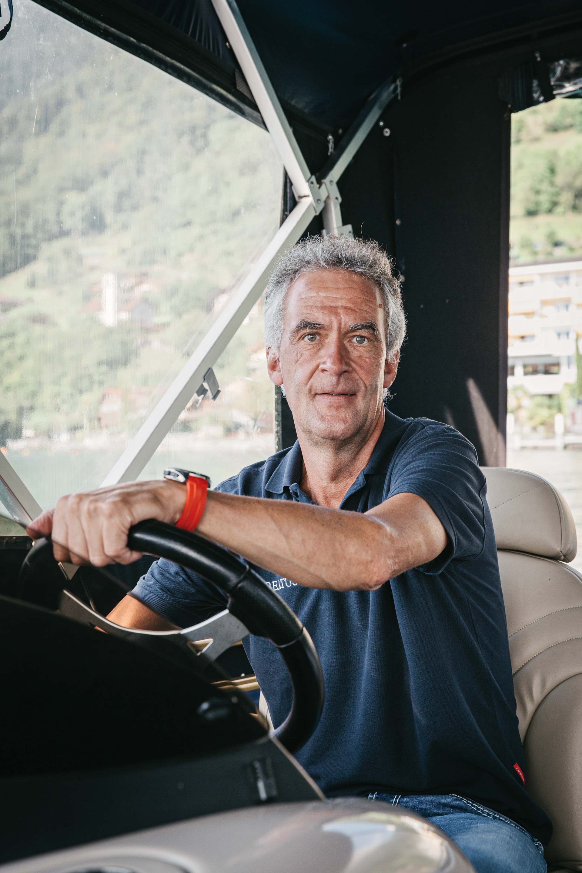 Un homme regarde directement la caméra, ses mains sont posées sur le volant d'un bateau couvert.