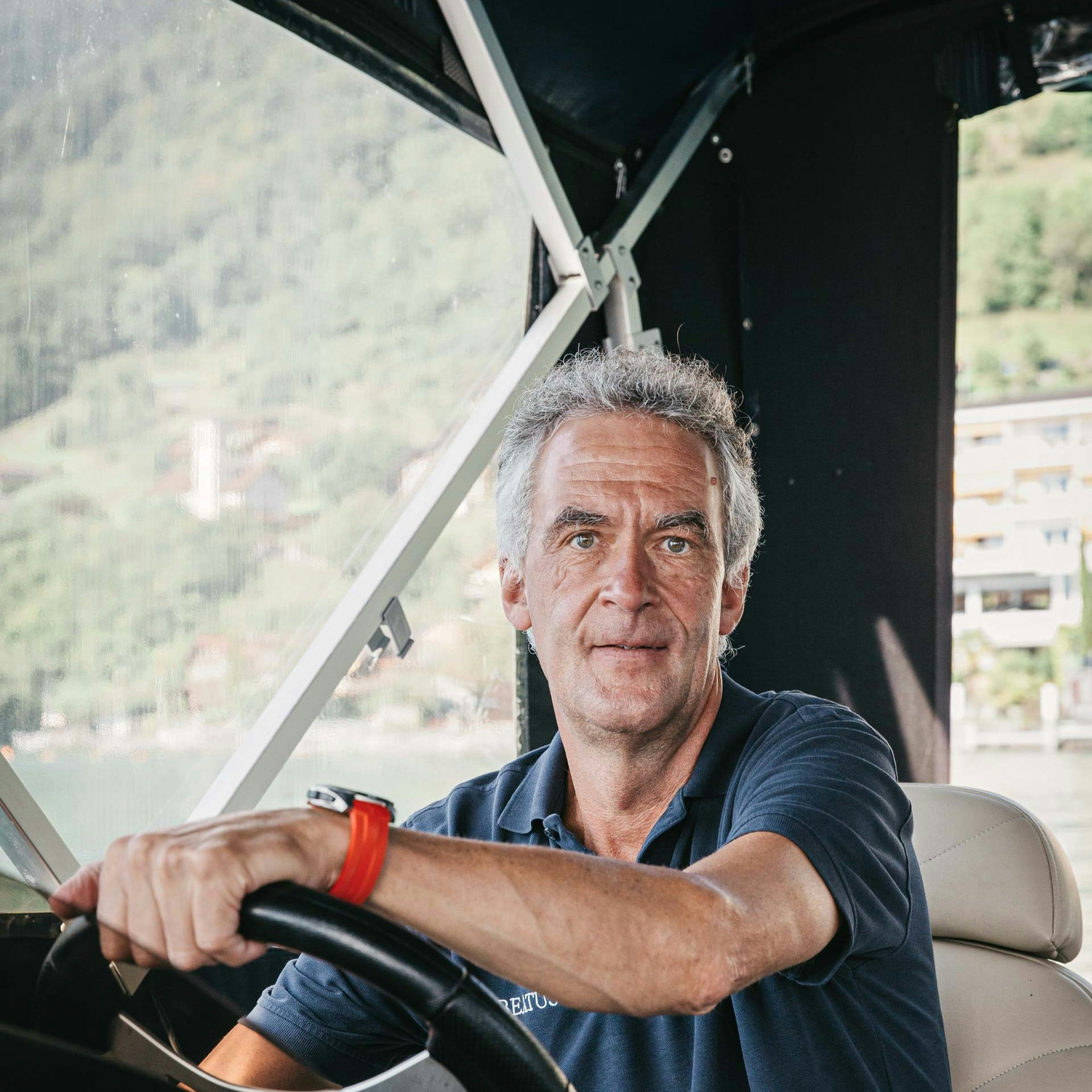 Volker Dietl is a nature guide at the Hotel BEATUS A man looks directly into the camera, his hands resting on the steering wheel of a covered boat