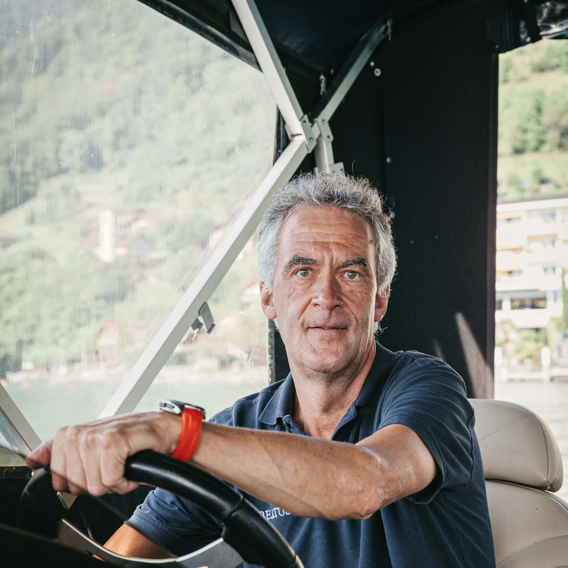 Volker Dietl est guide nature à l'hôtel BEATUS Un homme regarde directement la caméra, ses mains sont posées sur le volant d'un bateau couvert.