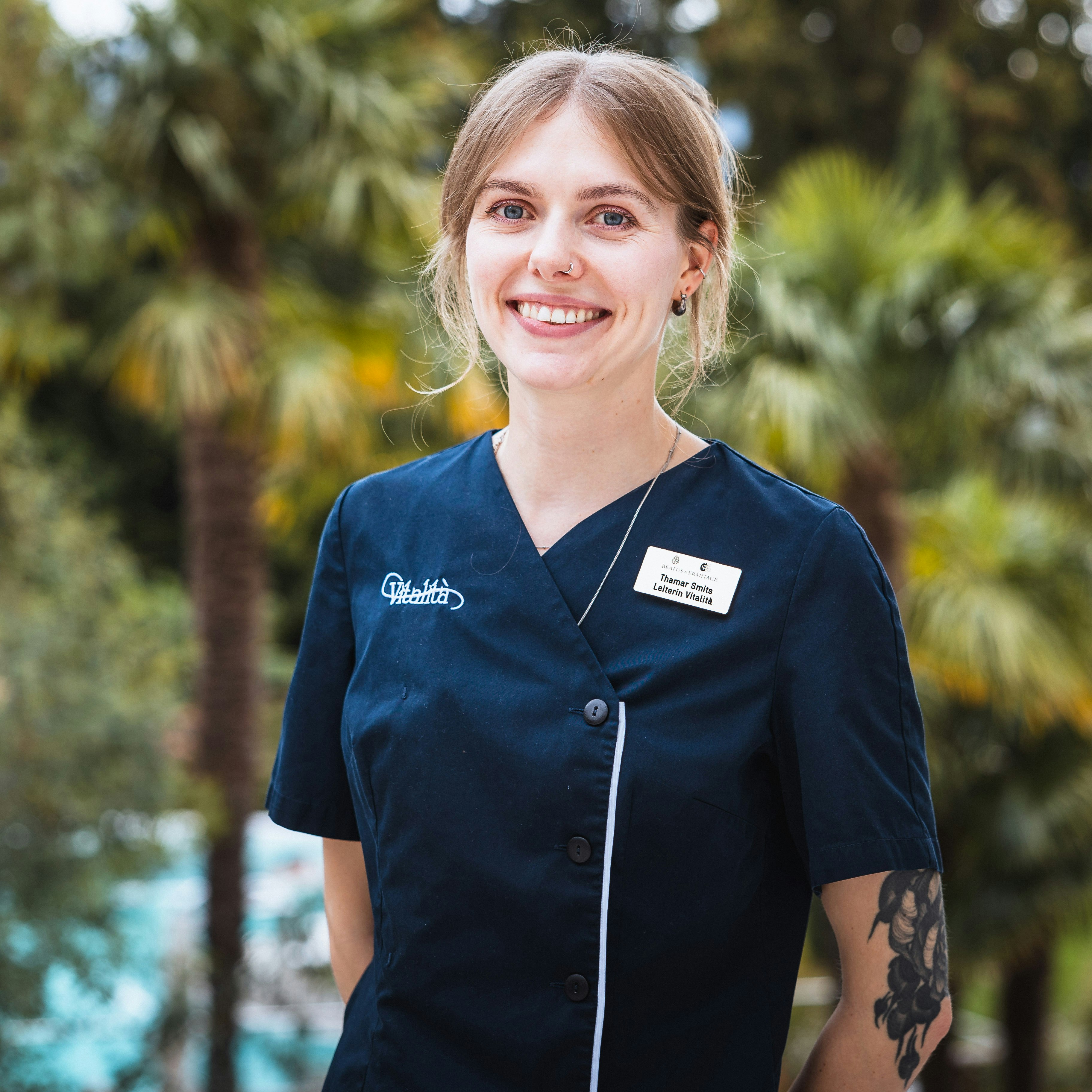 Thamar Smits, Head of Vitalità Smiling young woman in dark uniform with tattoos on her arm, palm trees