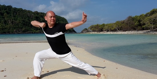 Mann auf Strand macht asiatische Kampfsportübung