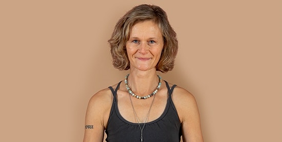 Nathalie Studer, yoga teacher at Hotel BEATUS Smiling woman with black T-shirt and necklaces, cropped against a brown background