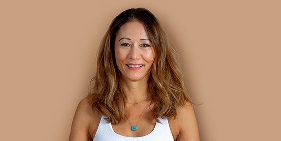Jacqueline Heinzmann, yoga teacher at the Hotel BEATUS Smiling, tanned woman with white T-shirt, cropped against a brown background