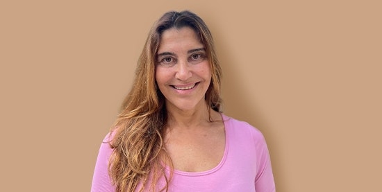 Martha Barthel, yoga teacher at Hotel BEATUS Smiling woman with pink T-shirt, cropped against a brown background