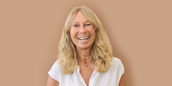 Mona Abter, yoga teacher at Hotel BEATUS Laughing woman with white blouse, cropped in front of brown background