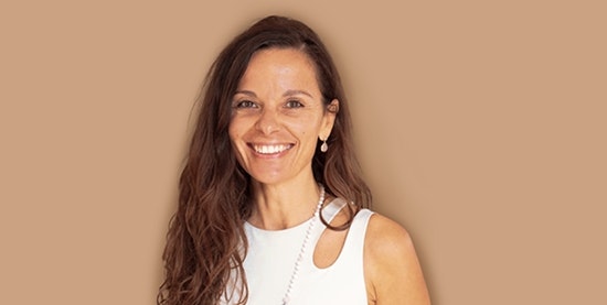 Maria Grazia Stomeo, yoga teacher at Hotel BEATUS Smiling woman in a white T-shirt, cropped against a brown background