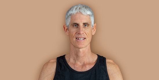 Matthias Brun, Yogalehrer im Hotel BEATUS Mann mit weissen Haaren und schwarzem T-Shirt, freigestellt vor braunem Hintergrund