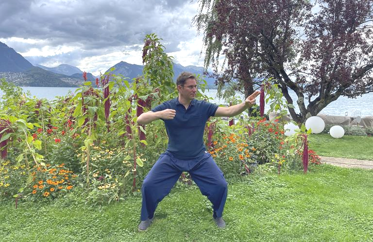 Man practising Qi Gong in a park, with the lake behind him