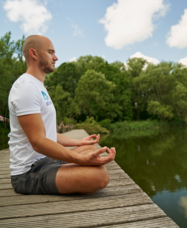 Young man sitting cross-legged on a wooden footbridge over a lake