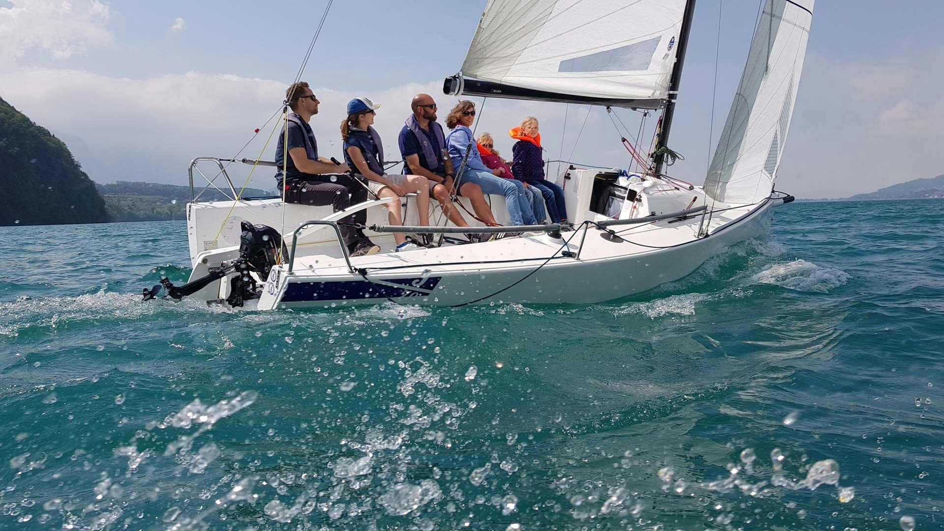 Ein Segelboot mit vier Erwachsenen und zwei Kindern von der Wasseroberfläche aus gesehen