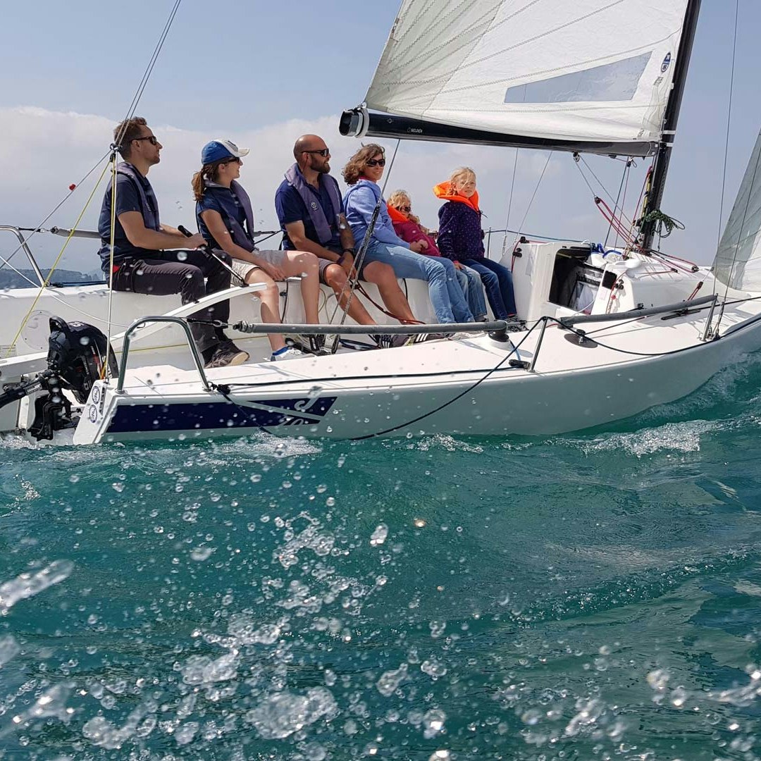 Segelkurs mit der Segelschule Thun Ein Segelboot mit vier Erwachsenen und zwei Kindern von der Wasseroberfläche aus gesehen