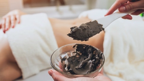 Peat pack Someone is mixing a brown paste, in the back a woman is lying on a massage table, covered with bath towels