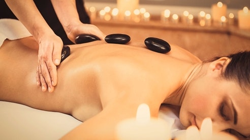 Massage aux pierres chaudes Des pierres chaudes sont posées sur le dos d'une femme allongée sur le ventre.