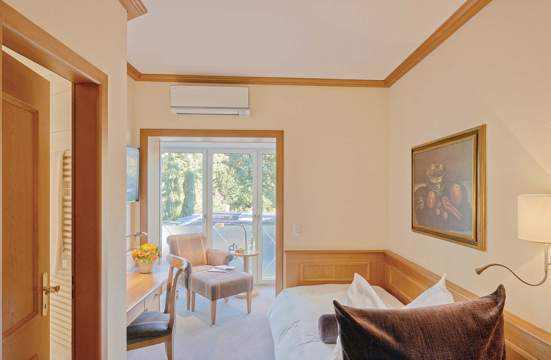 Blick von oben in ein Zimmer mit Teppichboden, Einzelbett, Schreibtisch mit Stuhl, Polstermöbel und Glasfenster