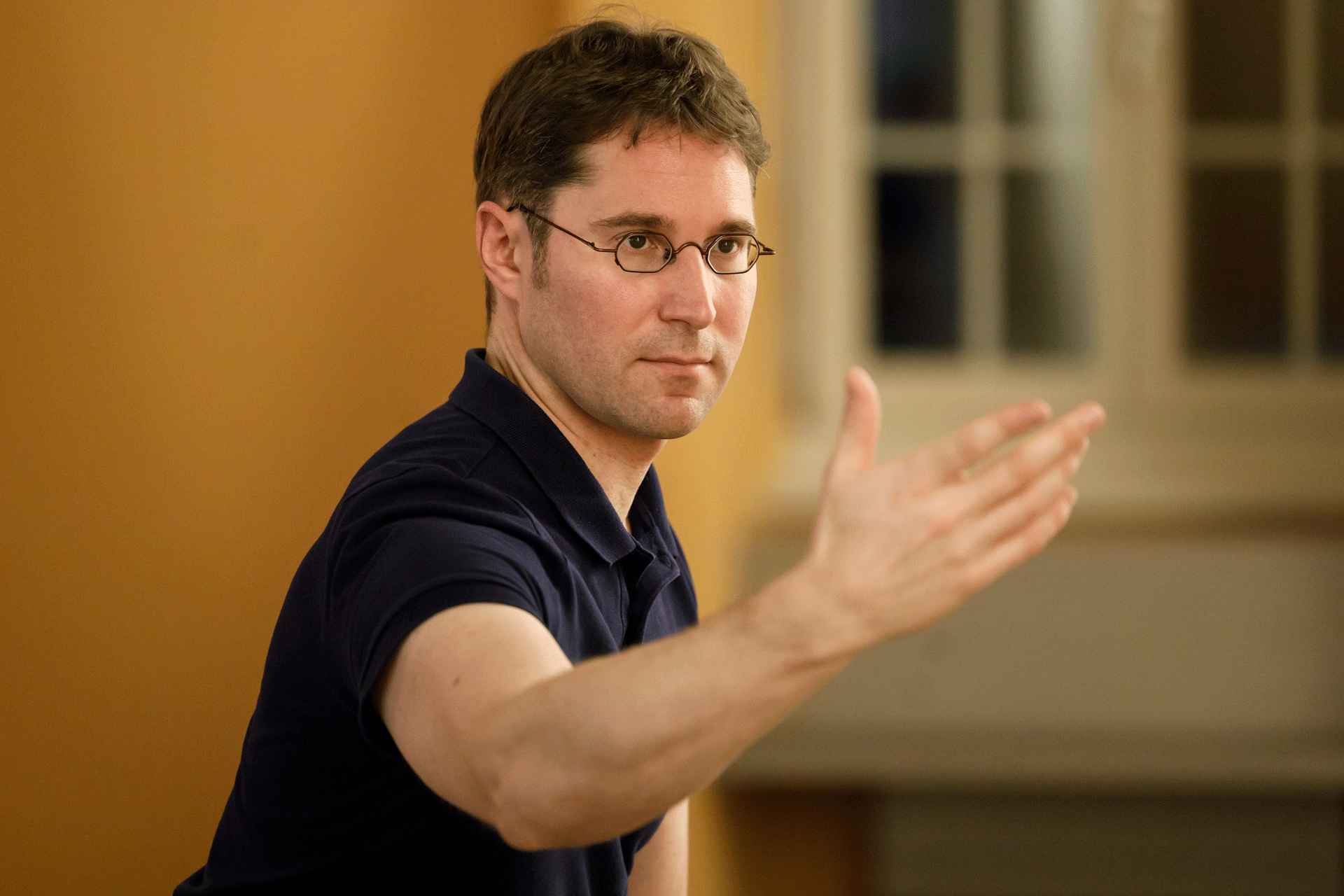 A man with glasses demonstrates a Qigong exercise