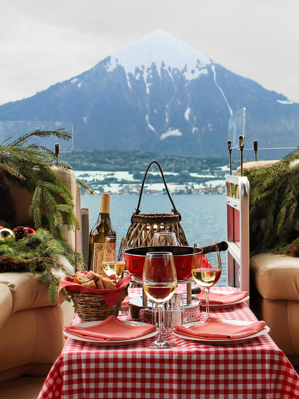 Fondueboot im Winter Ein offenes Boot mit Kunstlederbänken und weihnachtlicher Dekoration, auf einem Tisch Fondue, hinten ein Berg
