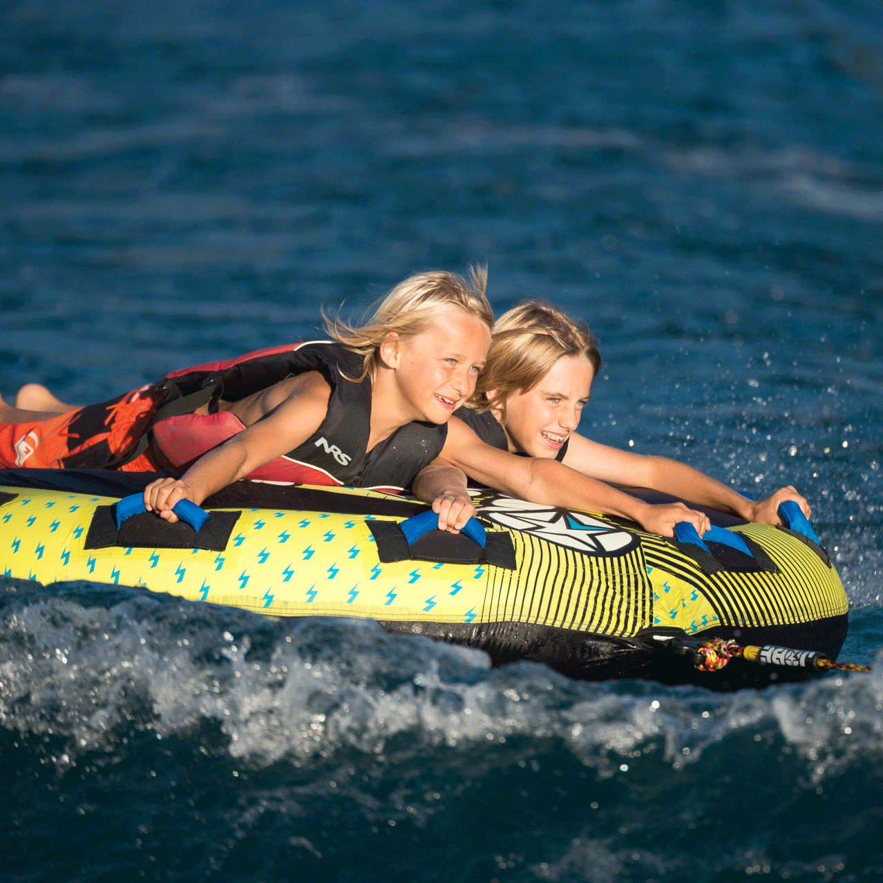 Funtube im Hotel Beatus Zwei lachende Kinder liegen auf einem grossen Gummireifen im Wasser und lassen sich von einem Boot ziehen
