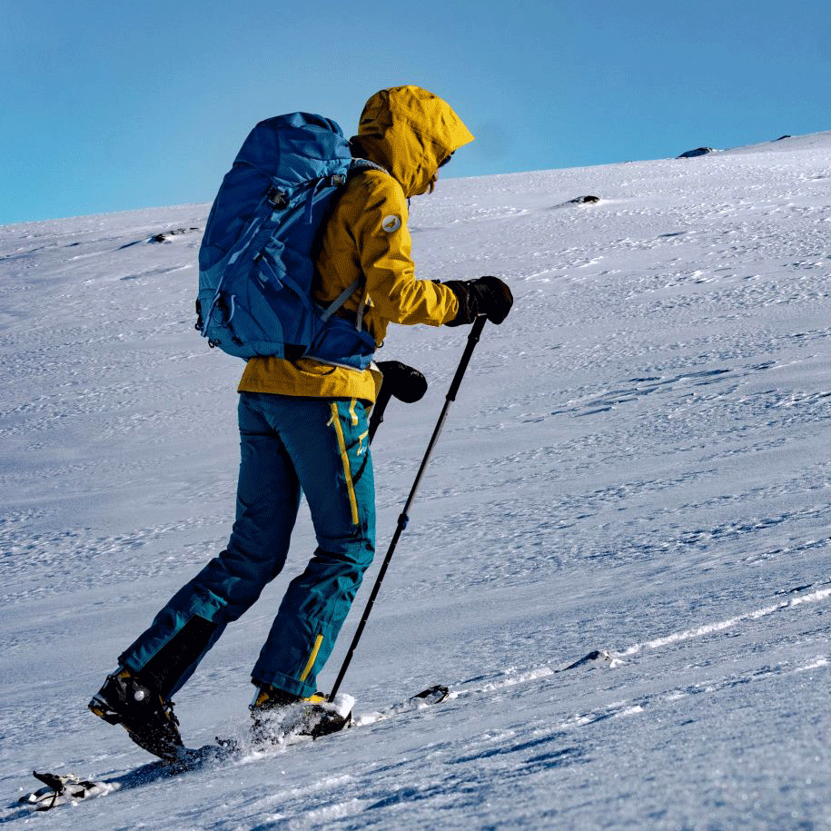 Ski de randonnée Un homme en anorak jaune et avec des bâtons de randonnée gravit une montagne enneigée