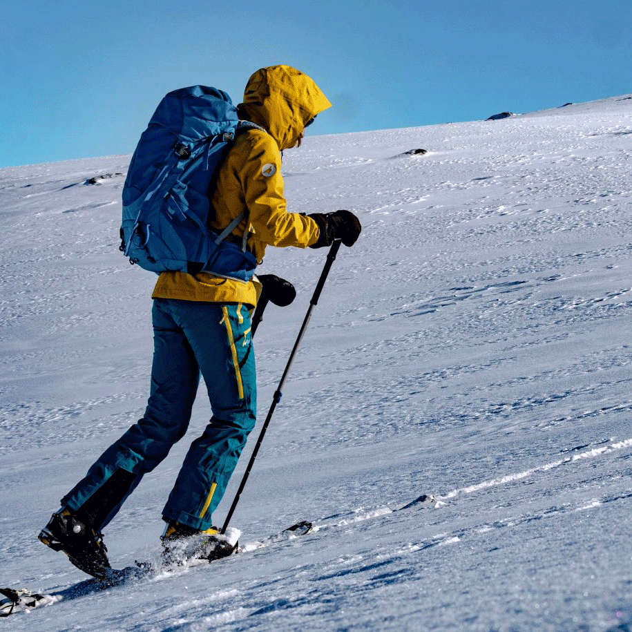 Touring skis Man in a yellow anorak and with hiking poles walks up a snow-covered mountain