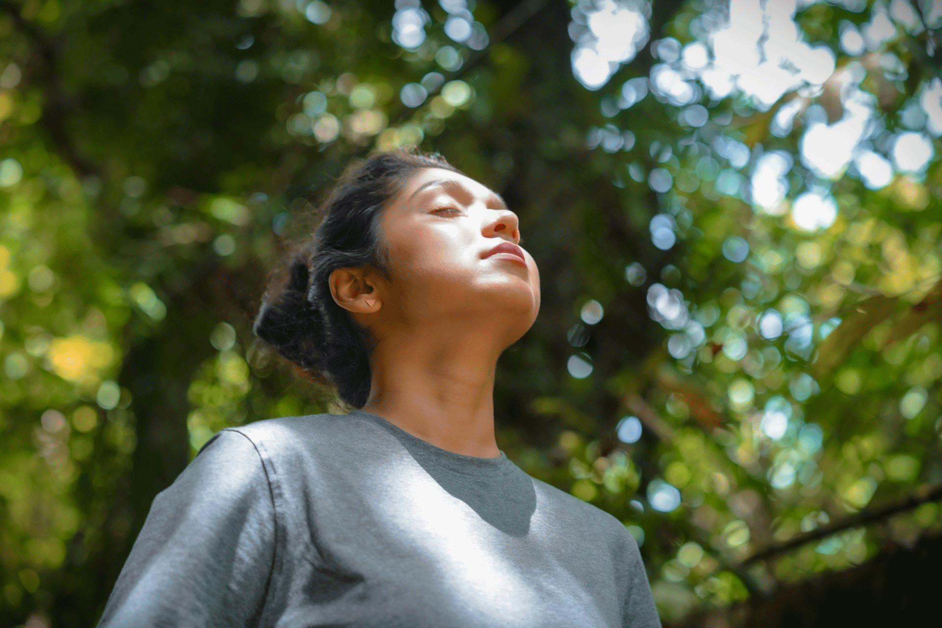 Woman stands in the forest and lets the sun shine on her face
