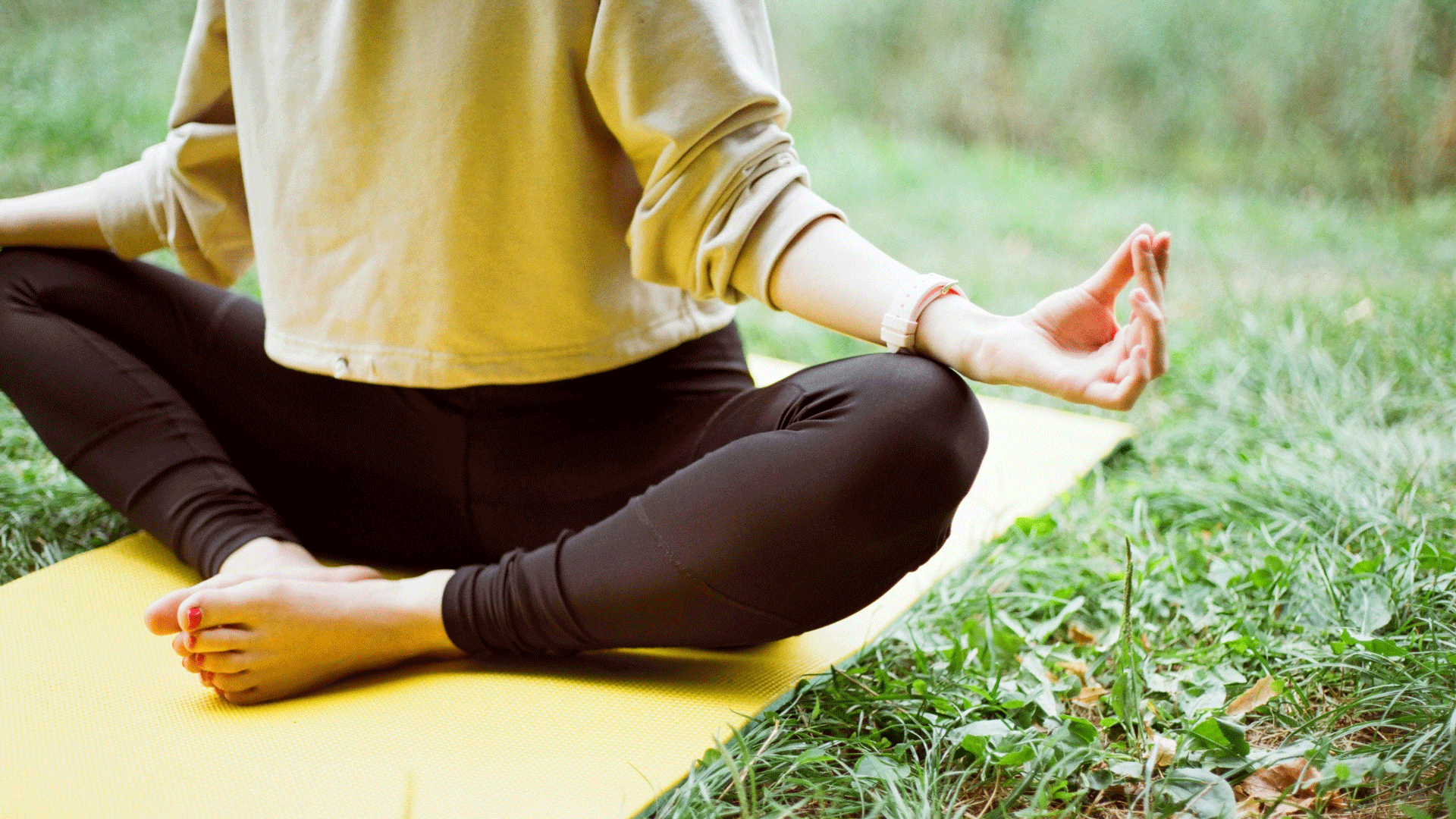 Retraite de méditation à l'hôtel Beatus Femme en pull jaune assise sur un tapis de yoga jaune dans la verdure, les doigts dans une position de mudra