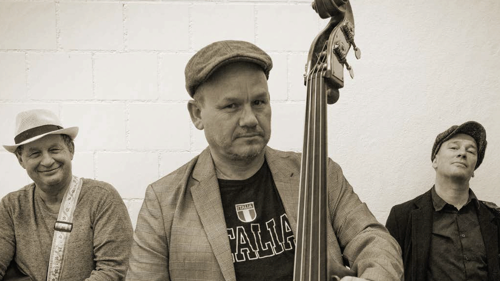 Veranstaltungsreihe im Hotel Beatus Foto in Sepiatönen von einem Musiktrio, in der Mitte im Vordergrund der Kontrabassist mit ernster Miene