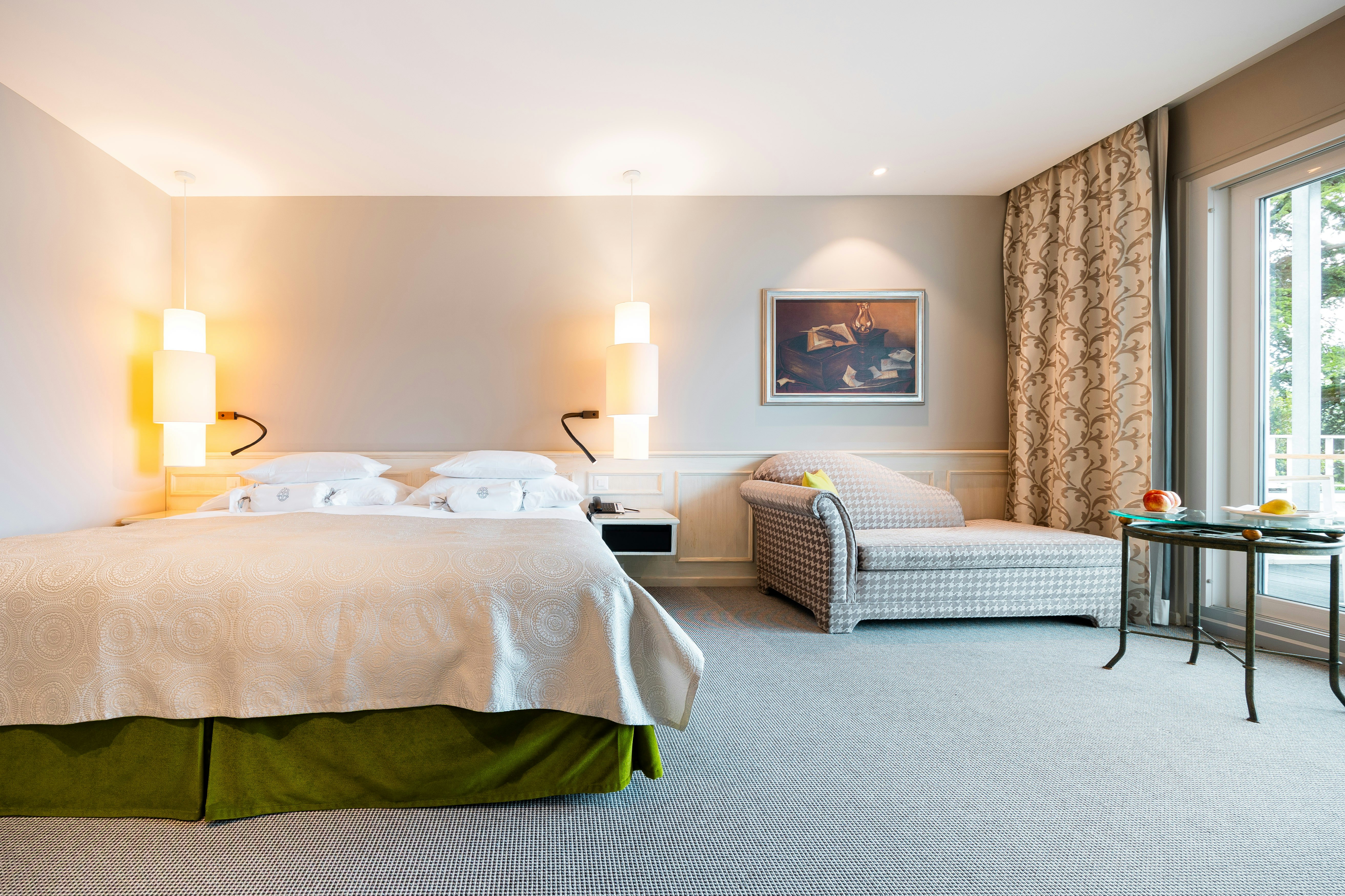 Zimmer mit Teppichboden, links ein Doppelbettt, rechts daneben ein Sofa und davor ein Tisch mit Früchten