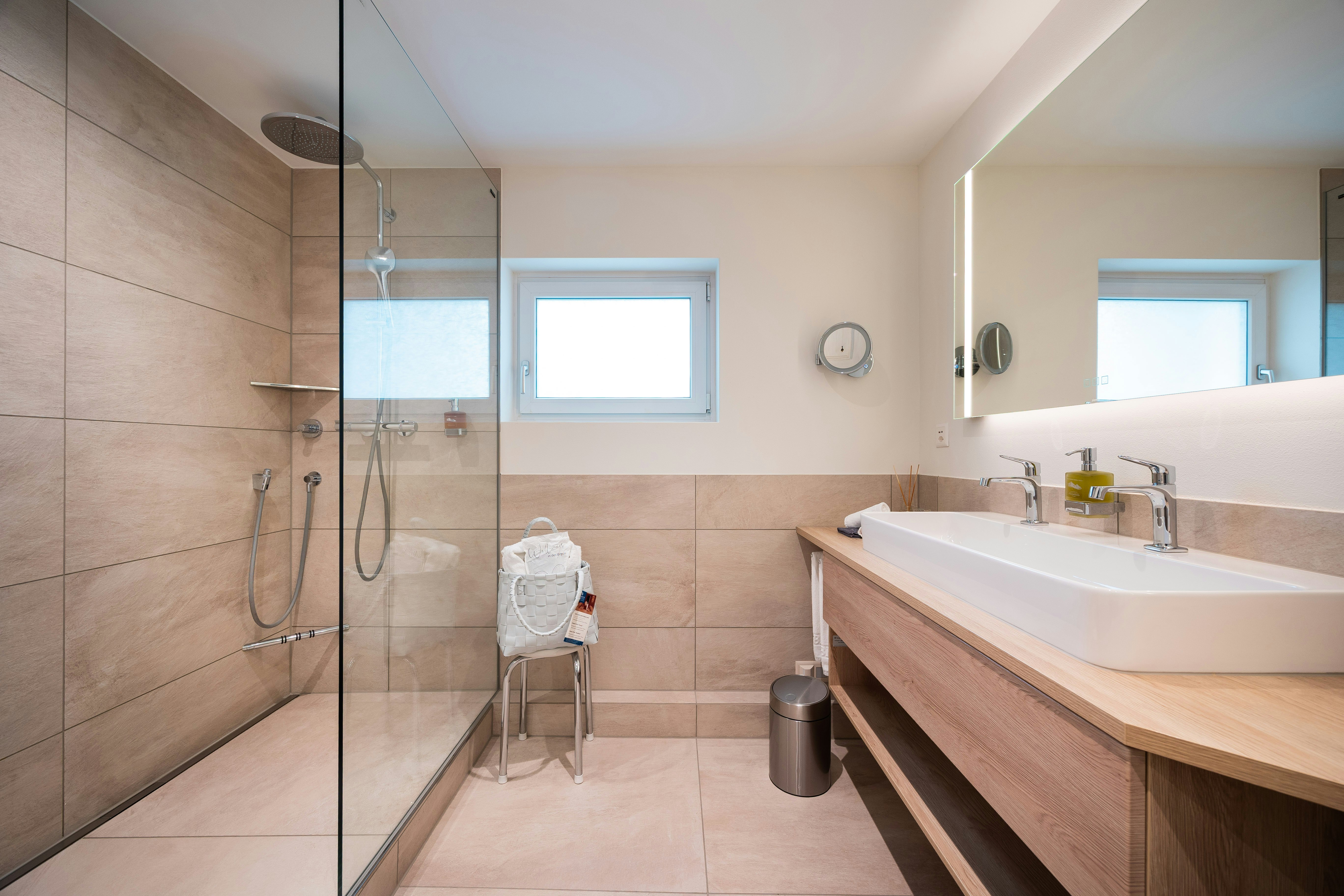 Links im Bild eine Dusche mit Absatz daneben ein Hocker und rechts davor ein Doppellavabo