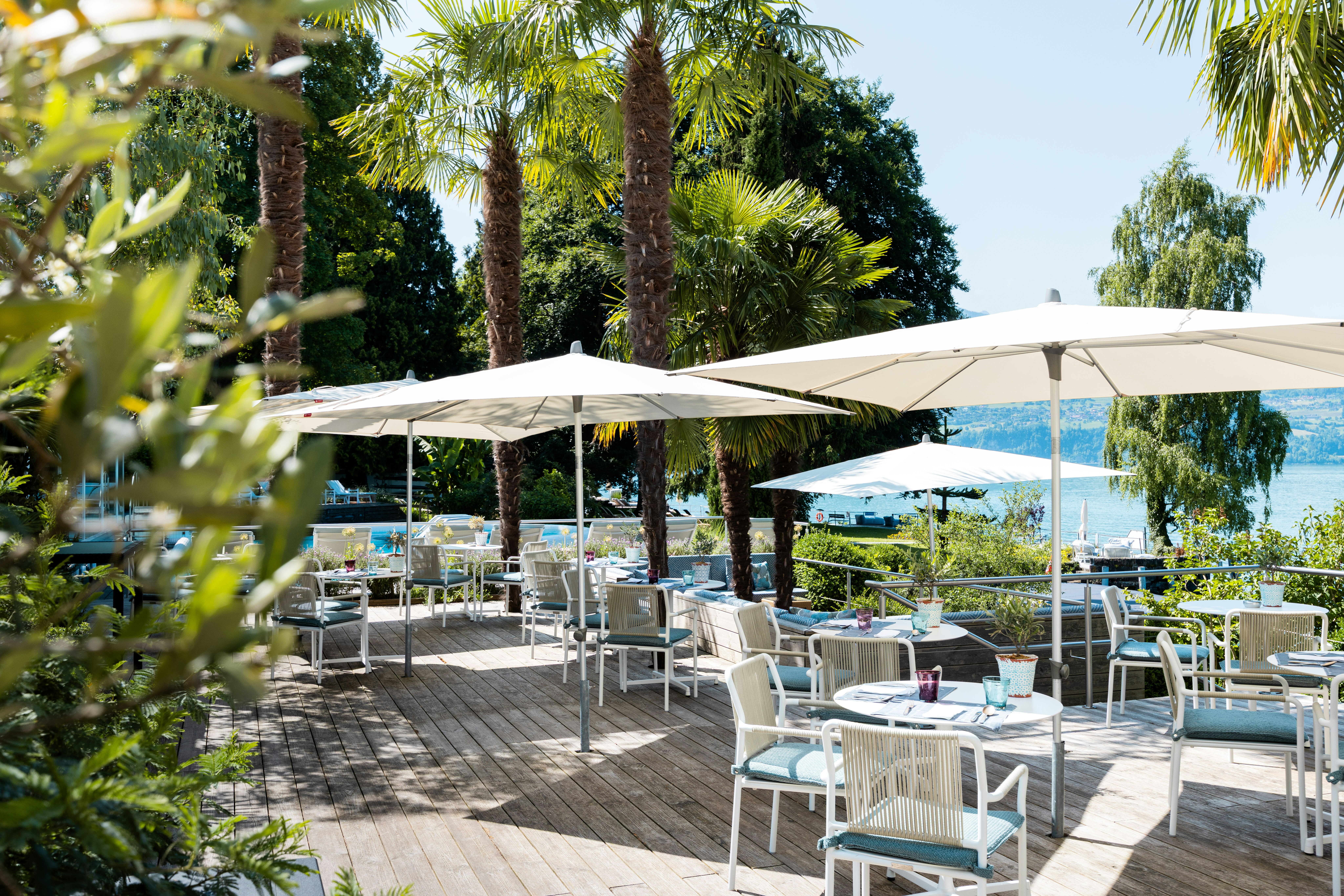 Set tables and open sunshades, with the lake and palm trees in the background.