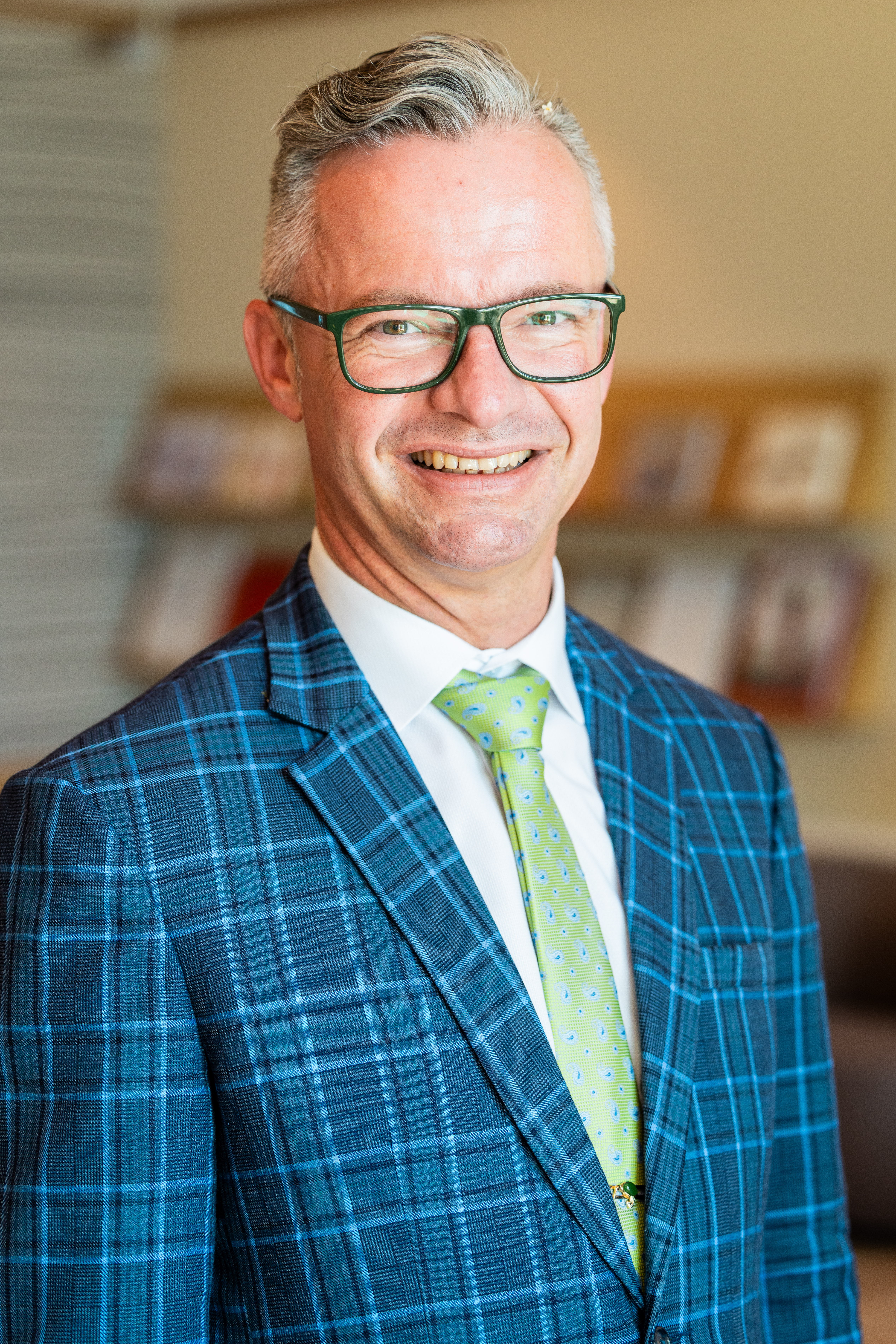 Mann mit weissem Hemd und kariertem Sakko, im Hintergrund unscharf ein Regal mit Magazinen