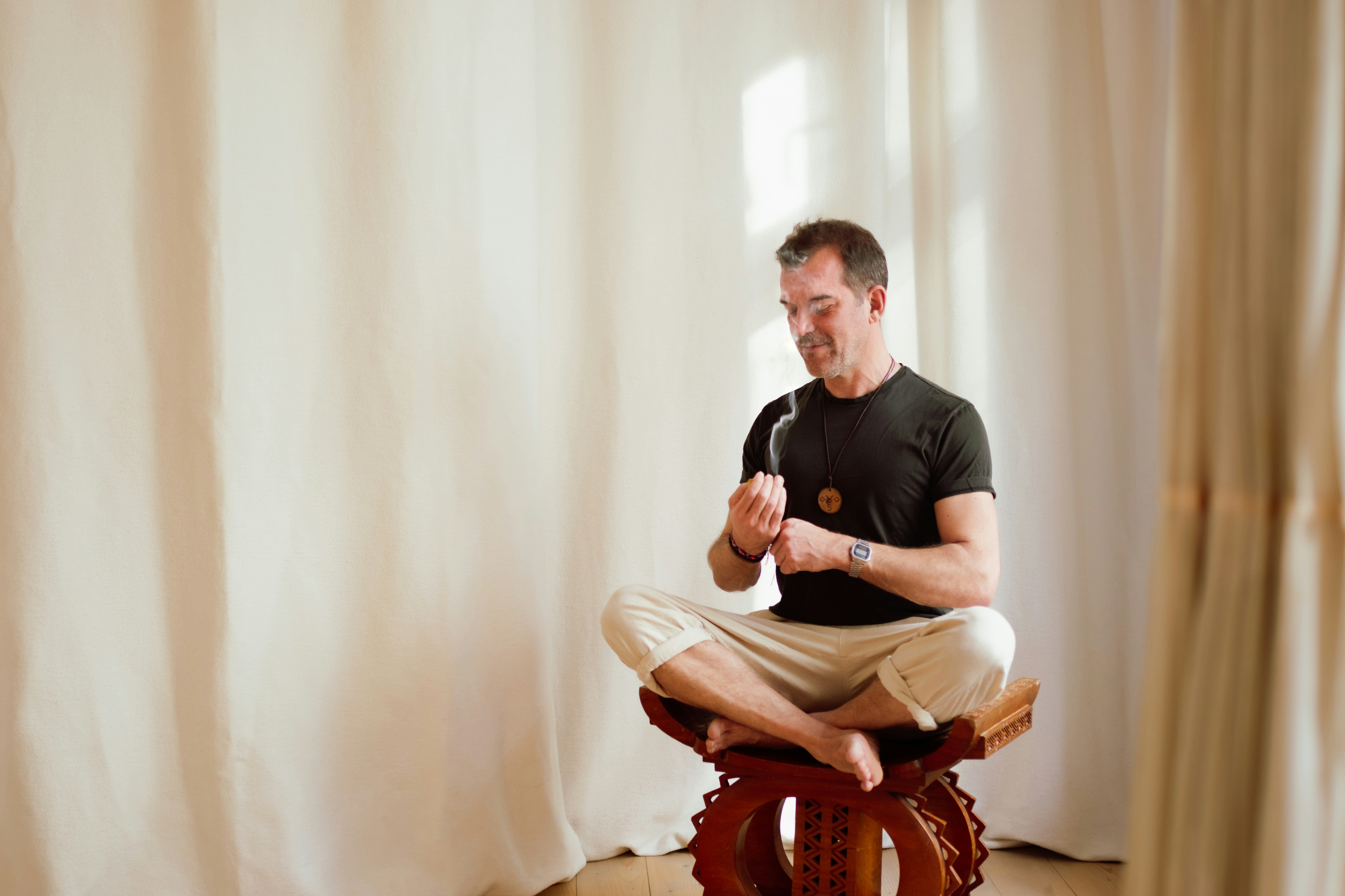 A man doing a breathing exercise, sits on a wooden chair.