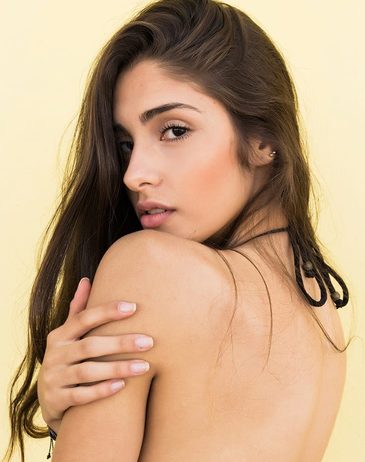 woman looking over her shoulder and touching her arm with her hand