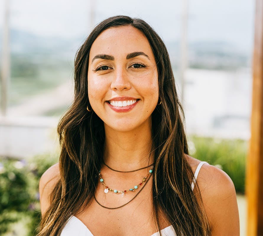 brunette haired woman smiling wearing beaded necklace while outside