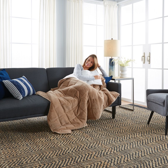 Woman smiling while sitting on her couch with a blanket