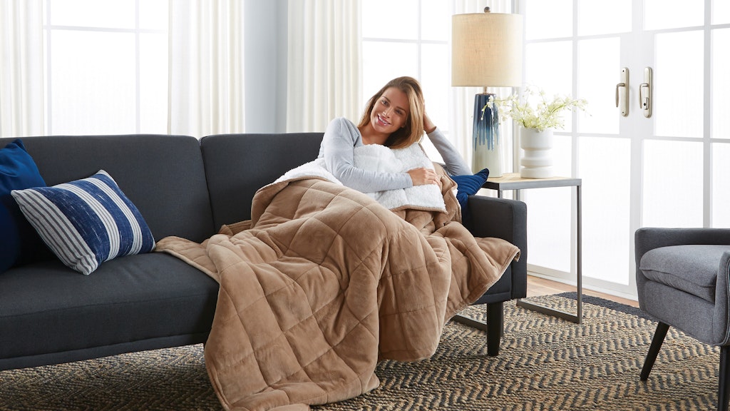Woman smiling while sitting on her couch with a blanket