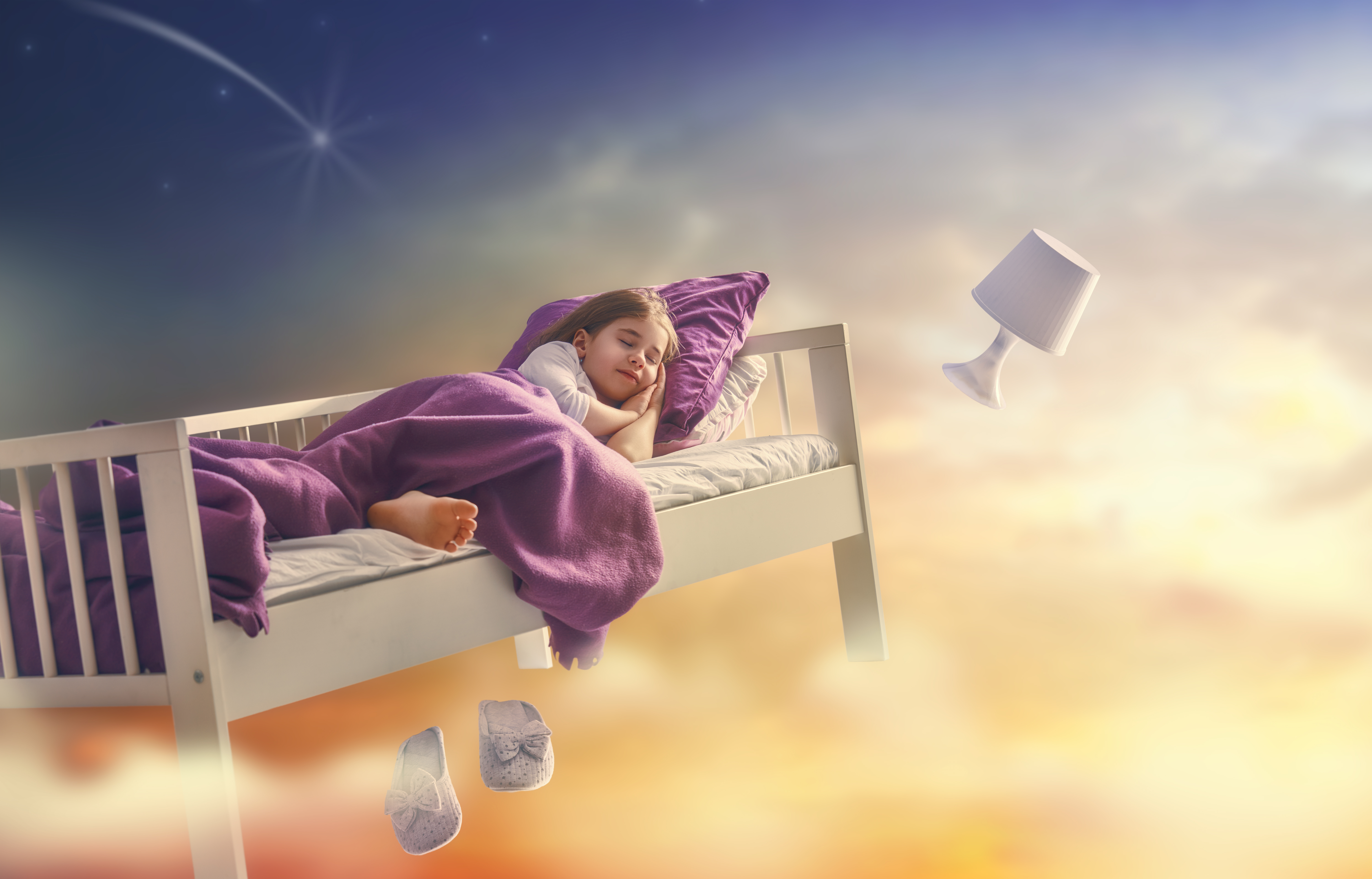 Image of a little girl alseep in her bed, drifting through the sky