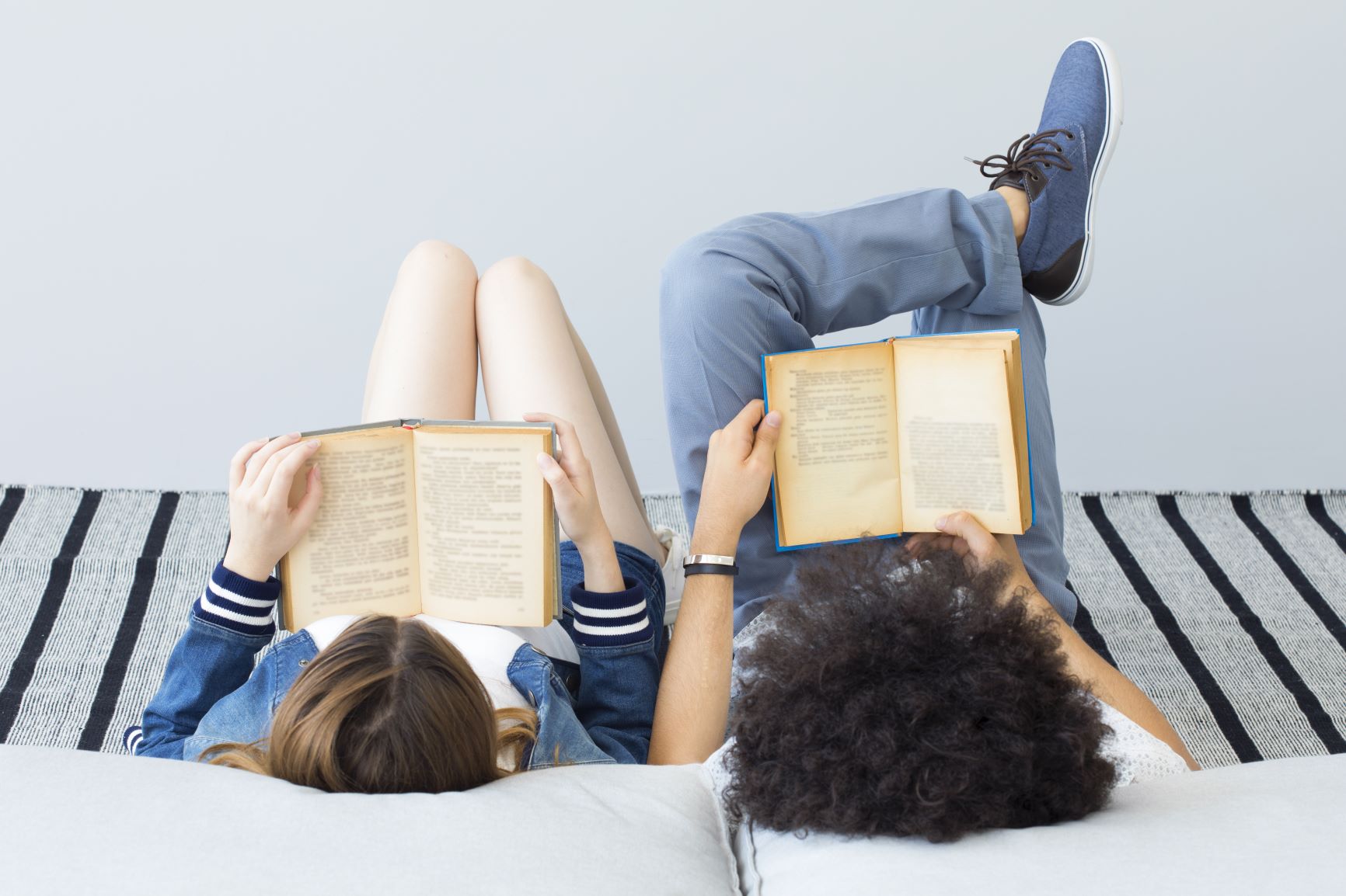 Two people laying in bed reading books