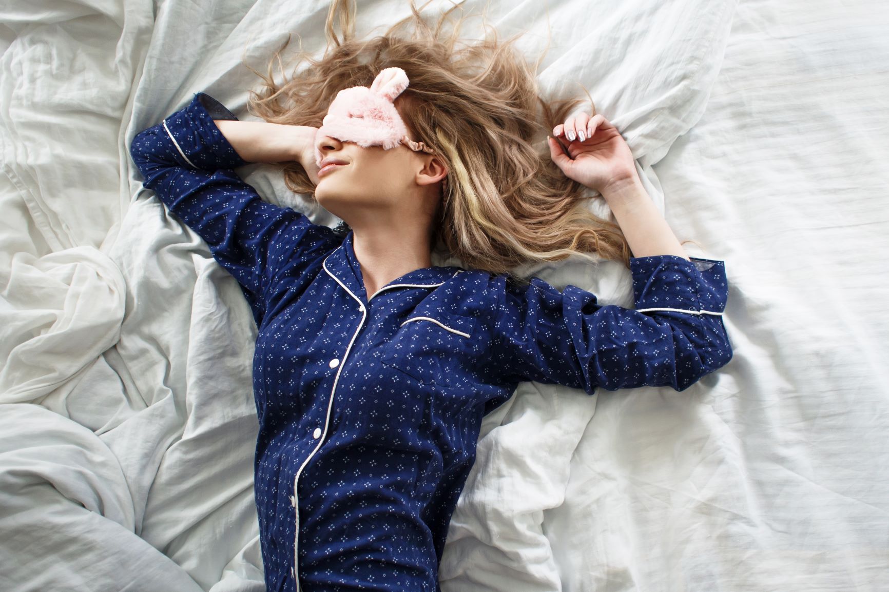 Woman asleep on her bed wearing a fuzzy eye mask