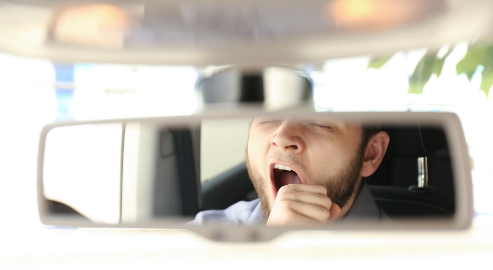 Photo of a rear view mirror reflecting a yawning driver