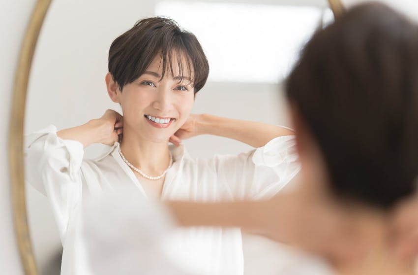 Woman putting on a necklace in a mirror