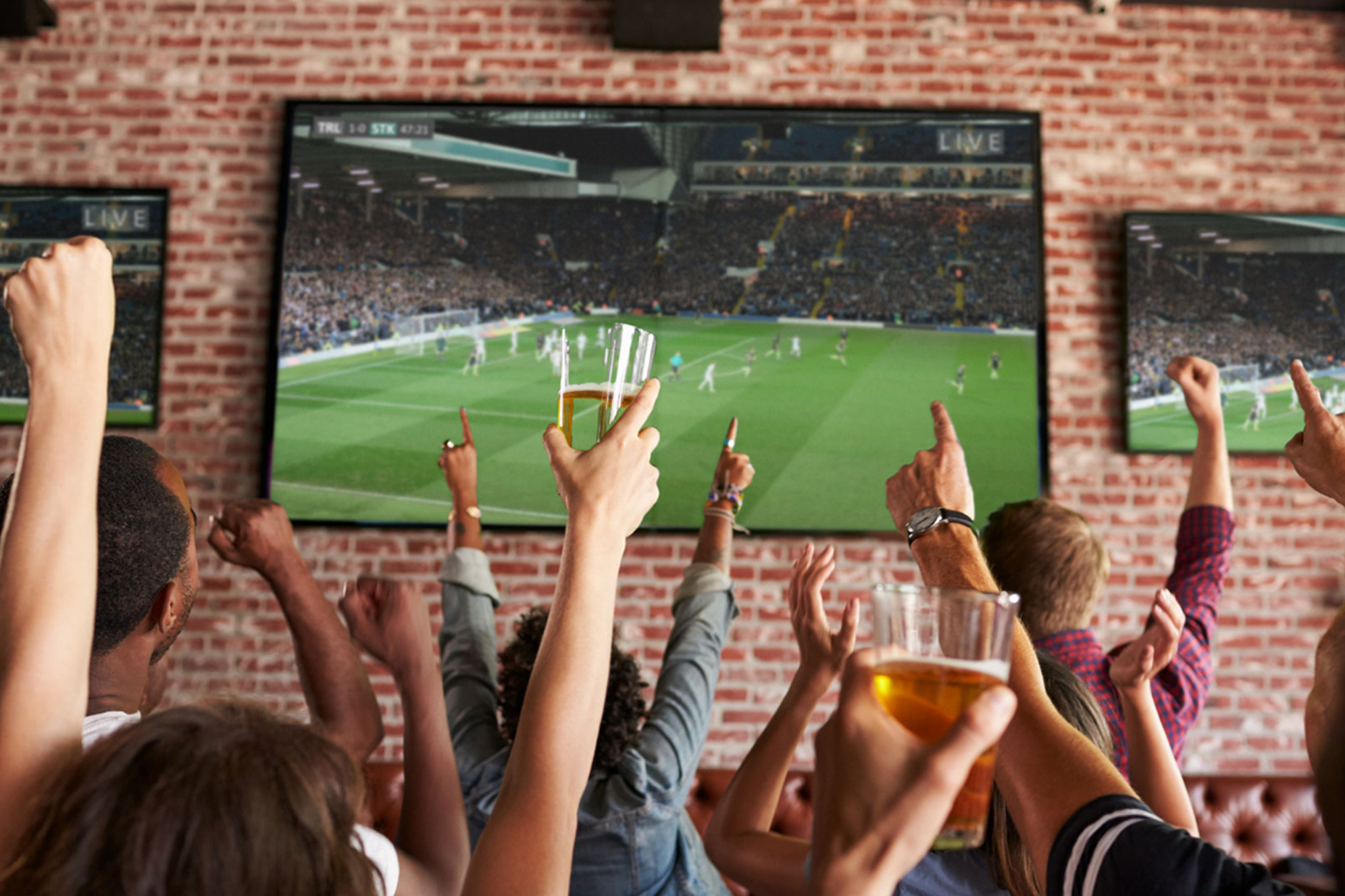 A group of people with their hands in the air cheering watching football on the TV
