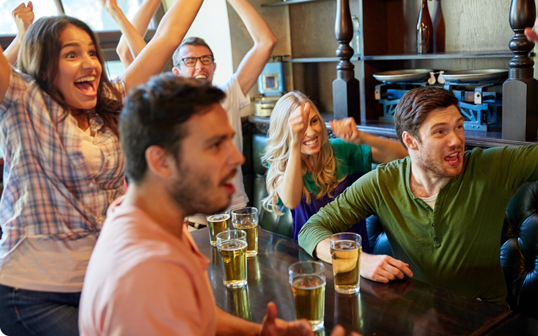 Crowd cheering inside a pub with pints on the table