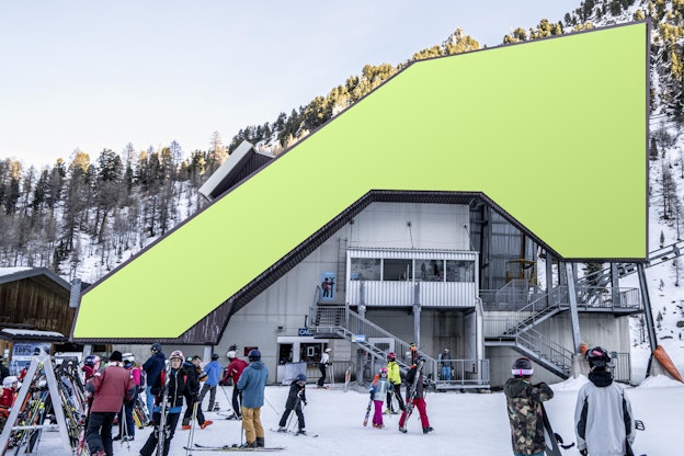 Skifahrer und Snowboarder versammeln sich vor einem Skigebiet am Fuße der verschneiten Pisten, mit einer großen grünen Form über dem Dach.