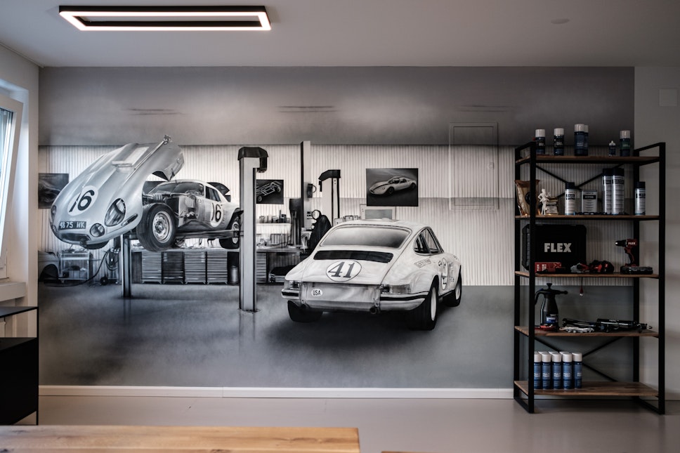 Eine Fototapete zeigt Oldtimer in einer Garage, auf der rechten Seite ein Regal mit Autoprodukten und Werkzeugen unter einer einfachen Deckenleuchte.