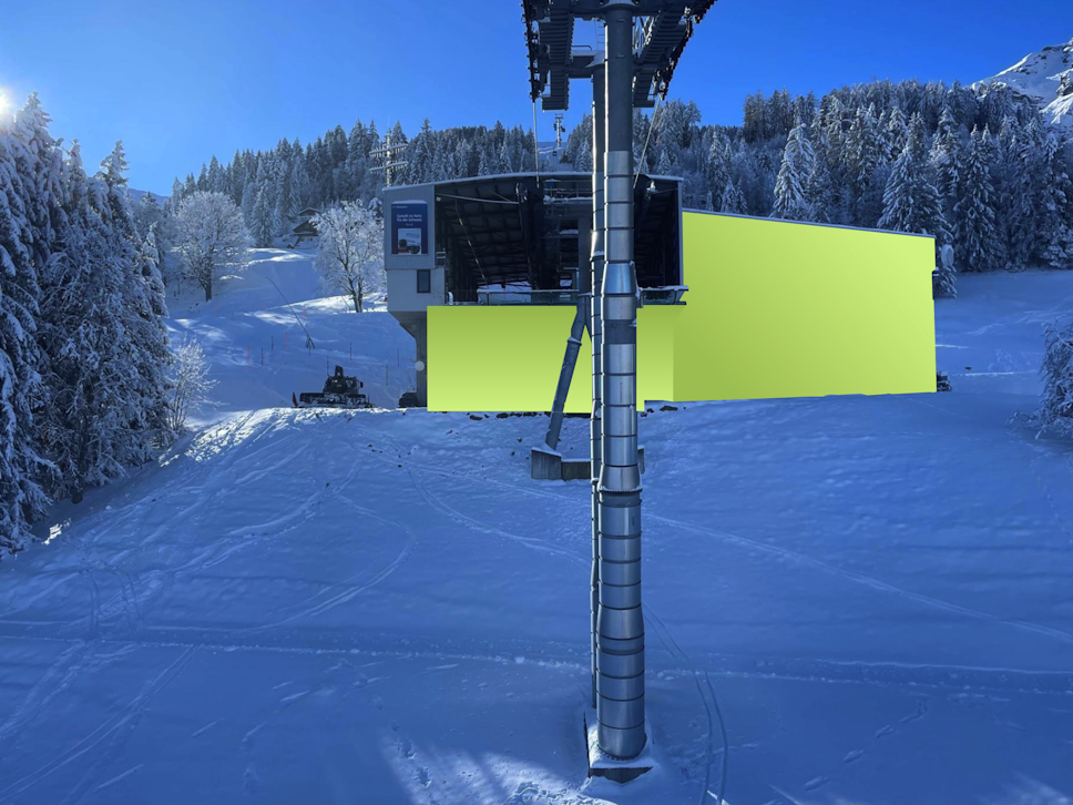 Ein Skiliftturm steht vor einer gelben Station, umgeben von verschneiten Bäumen und Pisten unter einem klaren blauen Himmel.