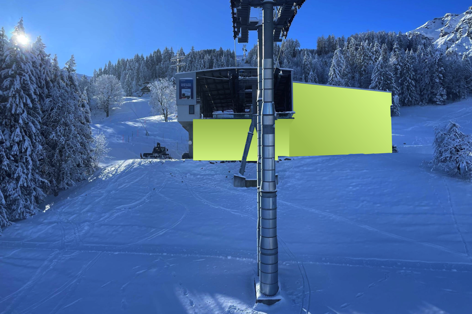 Ein Skiliftturm steht vor einer gelben Station, umgeben von verschneiten Bäumen und Pisten unter einem klaren blauen Himmel.
