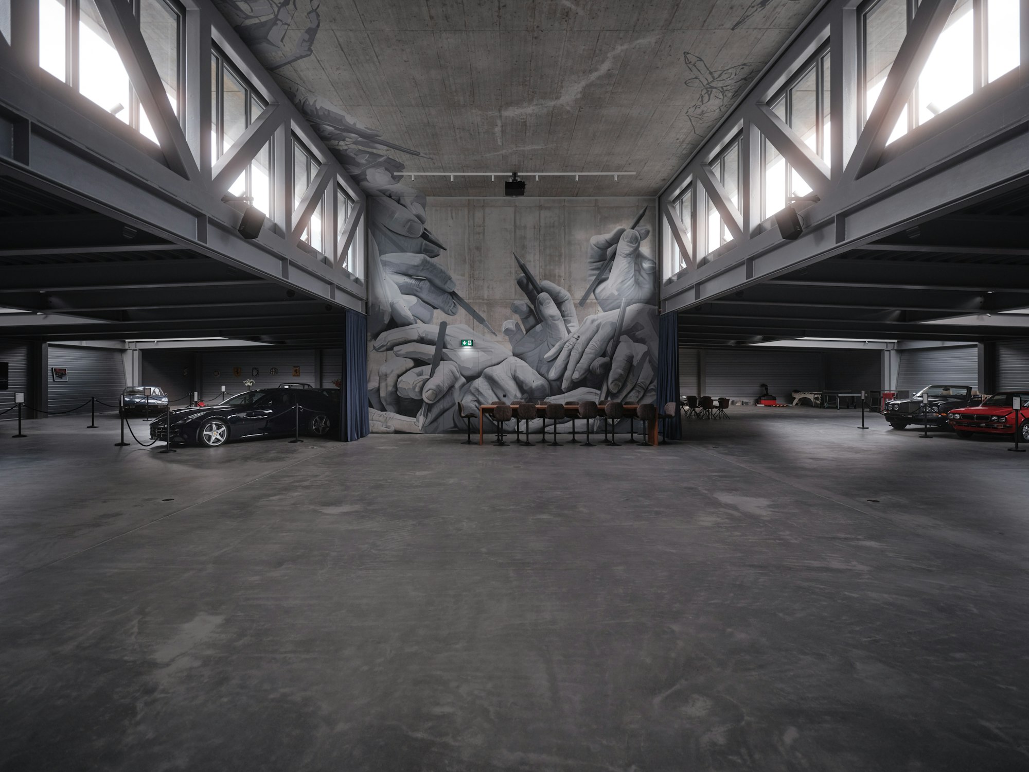 Eine geräumige Industriegarage mit geparkten Autos und einem Wandgemälde mit ineinandergreifenden Händen unter hohen Decken und großen Fenstern.