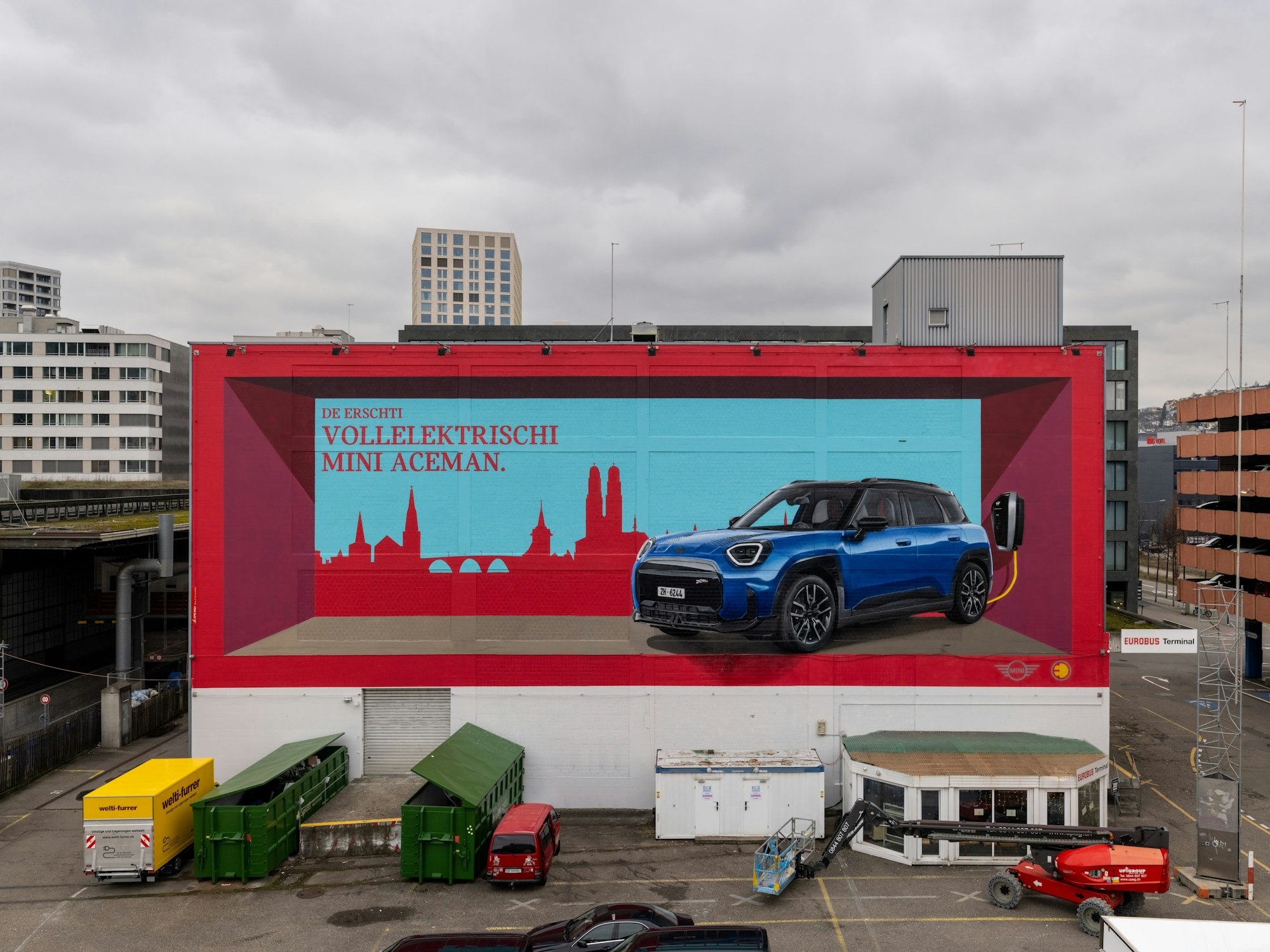 Grosses MINI Aceman Werbemural an Gebäudefassade (Hardbrücke) in Zürich mit Elektroauto und Stadtsilhouette, auffällige Markeninszenierung.