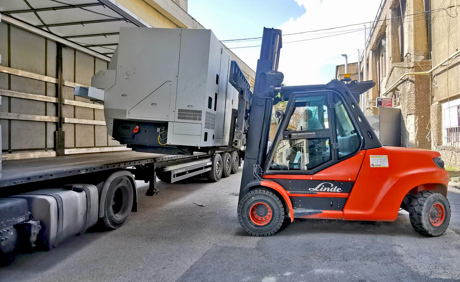 Ein Gabelstapler transportiert eine große Industriemaschine und lädt sie seitlich in einen Lkw.